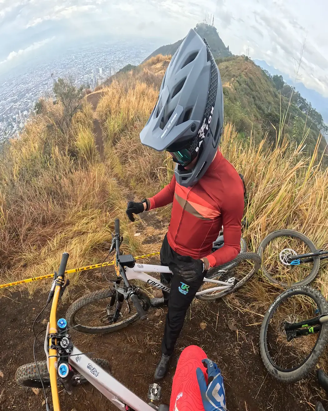 Juan Diego García del Club Trocha y Ruta, con casco integral gris y camiseta roja, se alista junto a las bicicletas en lo alto del Cali Bike Park, 2026