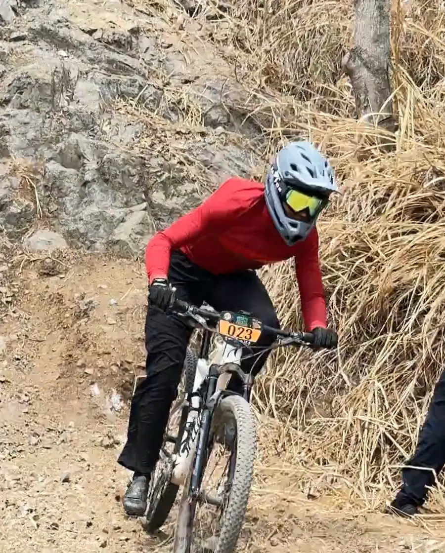 Juan Diego García del Club Trocha y Ruta, con casco integral y gafas, baja por un tramo de roca y pasto seco en su bicicleta, Copa Cali Bike Park, 2026