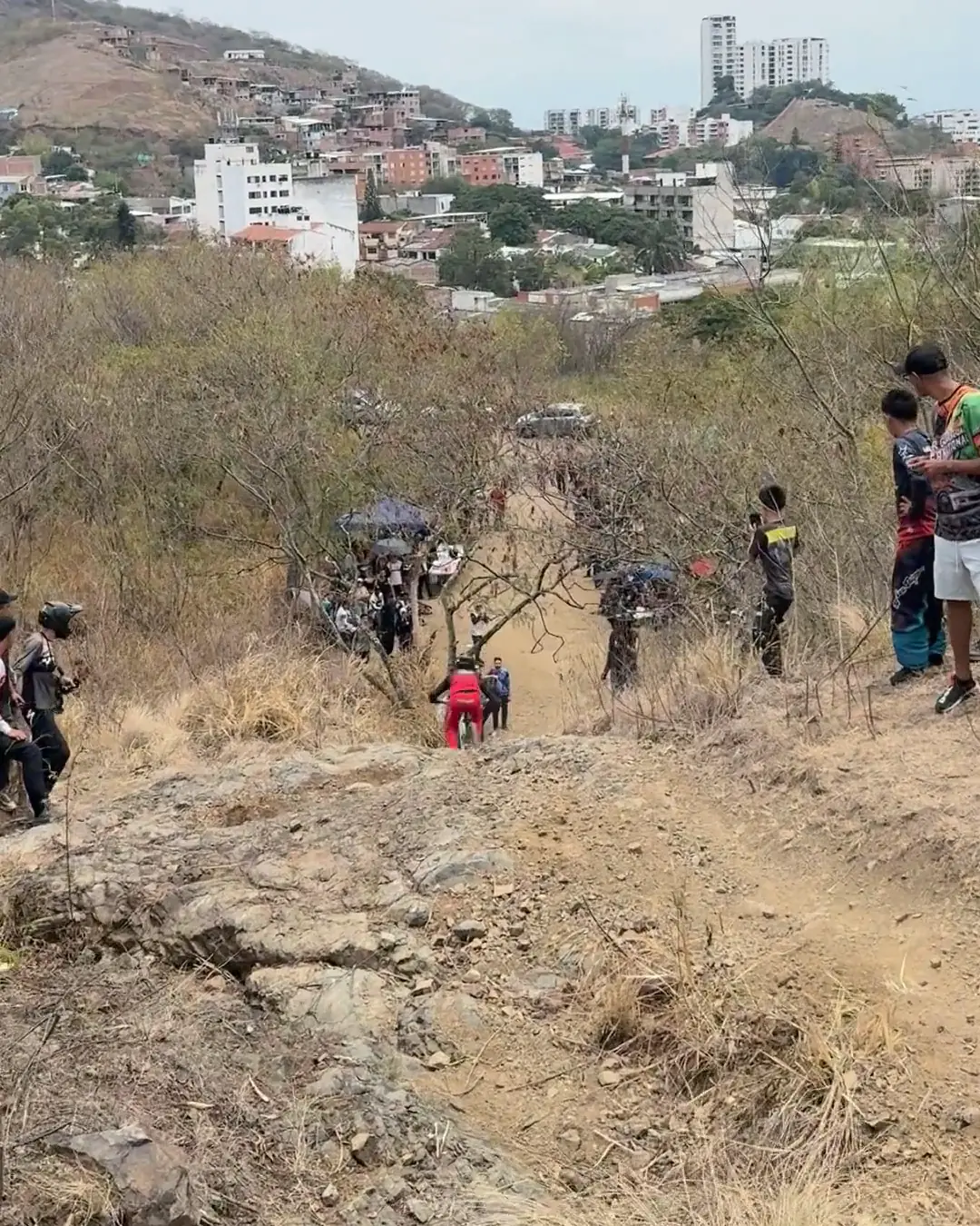 Juan Esteban Ortiz del Club Trocha y Ruta baja hacia la meta entre espectadores y sombrillas, con los edificios de Cali al fondo, en su segunda lanzada de la Copa Cali Bike Park, 2026