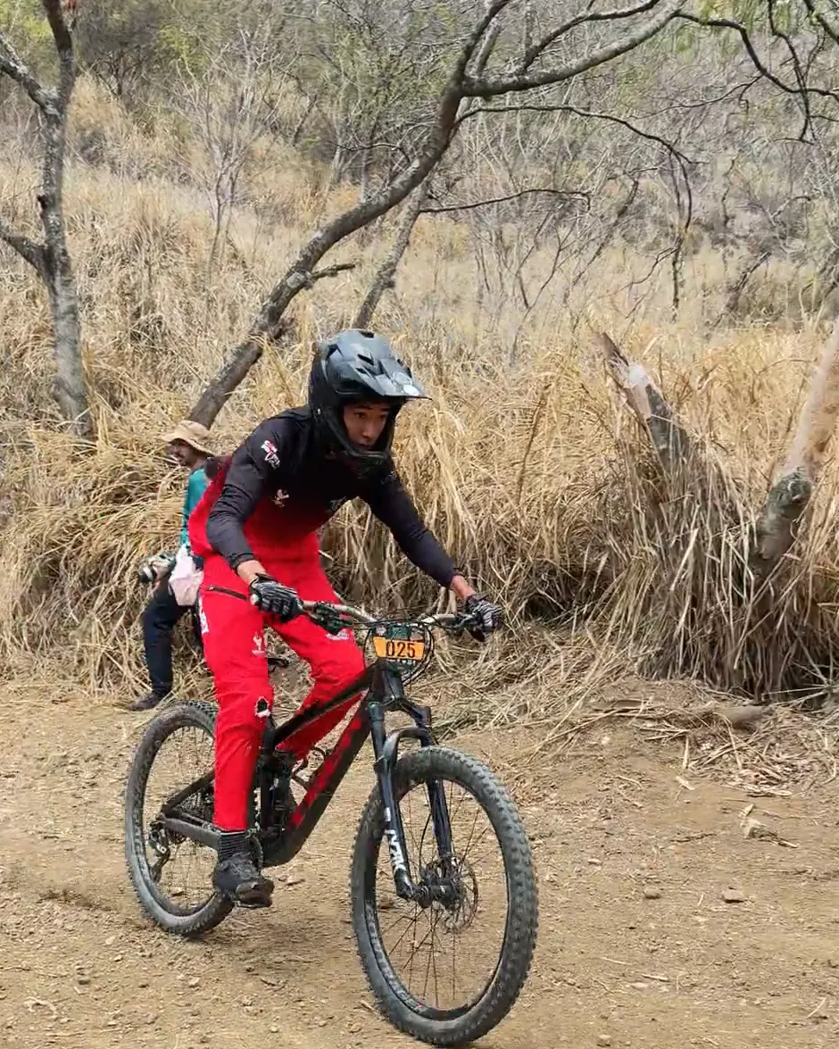 Samuel Ortiz del Club Trocha y Ruta llega en la bicicleta de descenso a la zona plana de la meta, entre árboles secos, Copa Cali Bike Park, 2026
