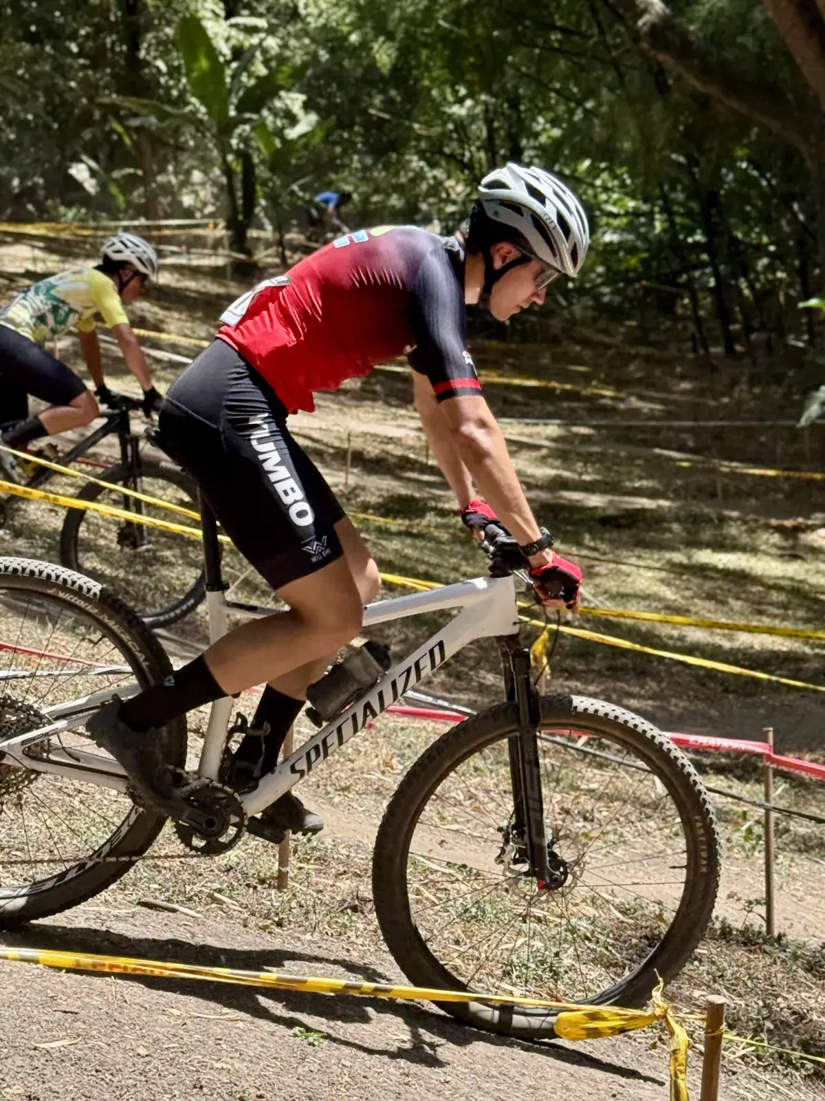 Juan Diego García inclinado sobre su bicicleta blanca Specialized, tomando una curva del circuito de XCO entre los árboles del Bosque Municipal